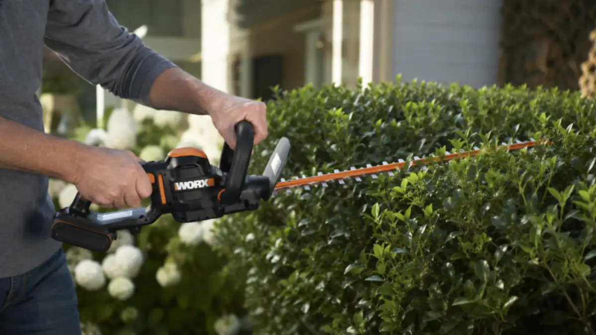 Hand pulling the trigger on the WORX cordless hedge trimmer while trimming a boxwood hedge